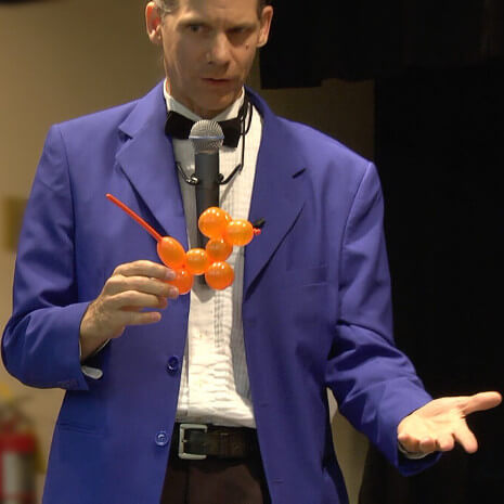 A boy helps the magician perform a balloon animal magic trick on stage in a Chicago magic program!